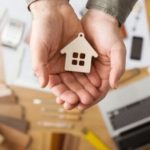 Hands holding a wooden house figurine with square cut-outs, symbolizing craftsmanship in home plumbing solutions.