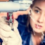Young plumber repairing a leak with a wrench, surrounded by exposed pipes indicating burst pipe issues.