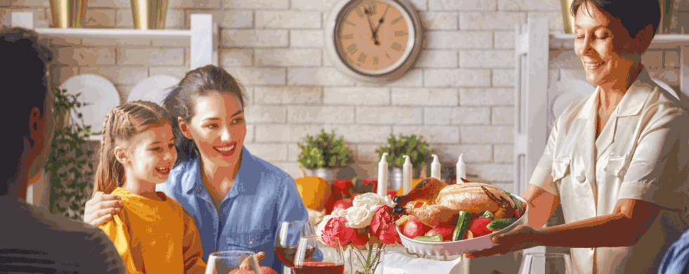 Family gathering at Thanksgiving dinner table with woman serving turkey, smiling children, and decorated setting.