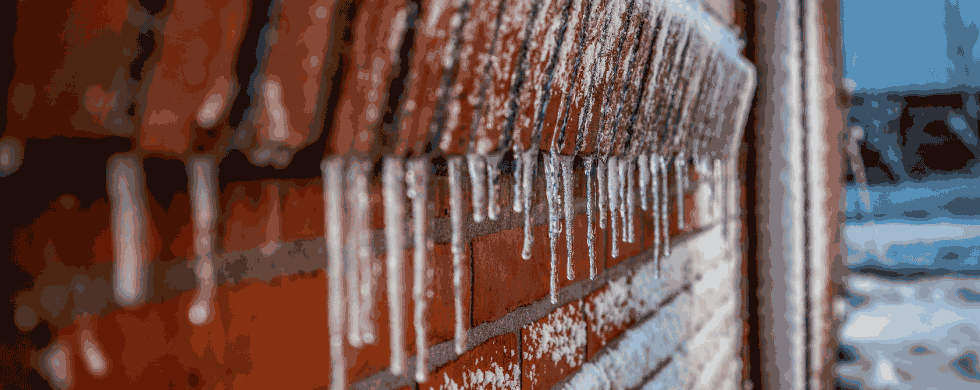 Icicles hanging from a red brick wall, illustrating winter conditions relevant for plumbing maintenance tips.