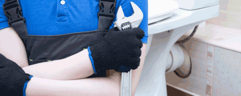 Plumber holding a wrench in front of a toilet, emphasizing plumbing services and maintenance.