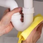 Close-up of hands cleaning a plumbing pipe with a yellow cloth for efficient water conservation by Marc Francis Plumbing.