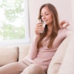 Young woman on a couch with a glass of water, highlighting Mark Francis Plumbing’s water filtration benefits.