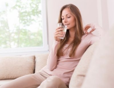 Woman enjoying a glass of clean water indoors, emphasizing the importance of water quality and filtration for health.