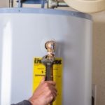 Water heater maintenance with a tool, showcasing a yellow instructional label by Marc Francis Plumbing for safe home care.