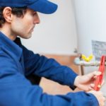 Technician from Marc Francis Plumbing repairing plumbing pipes and a water heater with tools in a blue uniform.