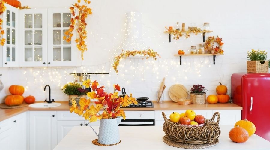 Autumn-themed kitchen with decorative pumpkins, vibrant fall leaves in a vase, and a basket of colorful fruits, reflecting seasonal home comfort and maintenance tips for homeowners.