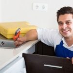 Technician smiling with tools in a modern kitchen, showcasing Marc Francis Plumbing's home improvement services.