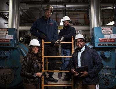 Adrienne Bennett and team of plumbing professionals in hard hats, posing in a commercial plumbing facility, showcasing diversity and teamwork in the plumbing industry.