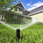 Lawn sprinkler watering a green lawn in front of a residential house by Marc Francis Plumbing for summer water conservation.