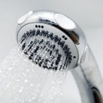 Shower head with chrome finish and water droplets, showcasing water-saving plumbing solutions from Marc Francis Plumbing.