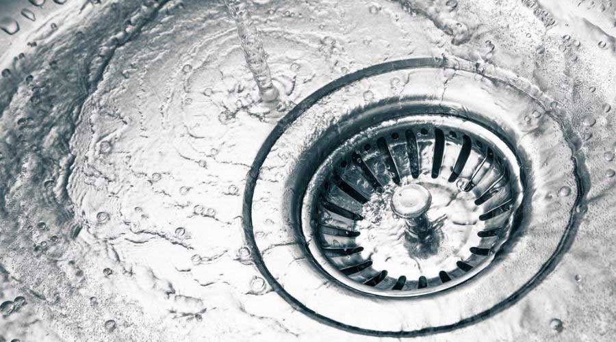 Kitchen sink drain with flowing water and circular grate; plumbing service by Marc Francis Plumbing for maintenance needs.