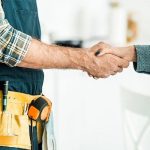Two plumbers shaking hands, one in a checkered shirt and apron, displaying professionalism for Marc Francis Plumbing.