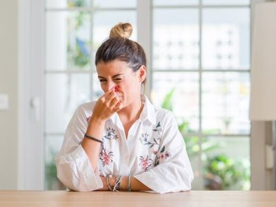 Woman grimacing and holding her nose, indicating a foul odor, in a home setting related to plumbing issues and sewage smells.