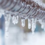 Icicles on a metallic pipe, illustrating risks of frozen pipes in winter. Marc Francis Plumbing services plumbing issues.