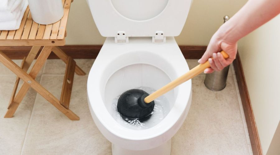 Person using a plunger in a toilet, demonstrating plumbing maintenance tips relevant to eco-friendly practices and home plumbing care.