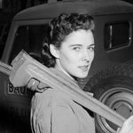Woman holding a wrench in vintage attire, beside an old vehicle, representing women's contributions in plumbing.