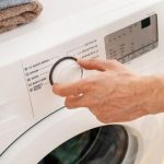 Washing machine with control panel, hand adjusting dial, and towels on top, promoting eco-friendly laundry practices.