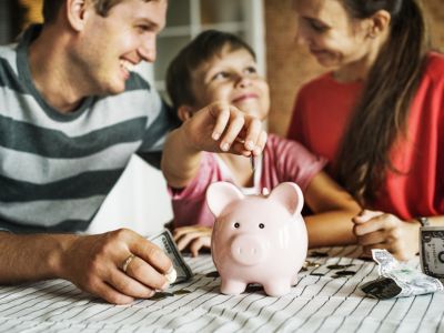 Family saving money in a pink piggy bank, illustrating financial benefits of water softeners for homeowners.