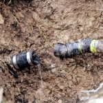 Broken water pipe connector leaking in muddy soil, highlighting sewer line issues, by Marc Francis Plumbing.