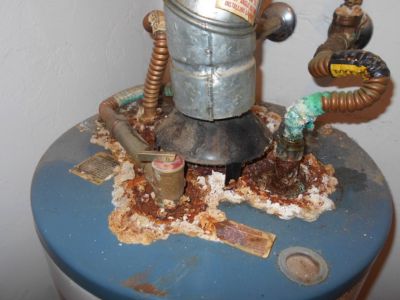 Corroded water heater tank with rust and mineral buildup, indicating the need for replacement due to neglect and potential water damage.