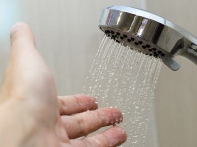 Hand reaching towards a showerhead with water flowing, illustrating potential hot water issues related to water heater performance.