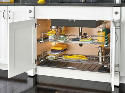 Open kitchen cabinet with organized storage, showcasing cleaning supplies and dishware, emphasizing the importance of allowing warm air circulation to protect plumbing during winter.