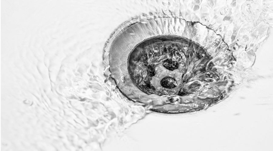Metal drain with flowing water, creating ripples and bubbles for plumbing maintenance insights at Marc Francis Plumbing.