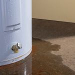 Water heater with visible leak and water pooling on the floor, indicating potential malfunction or need for replacement, relevant to plumbing services by Marc Francis Plumbing.