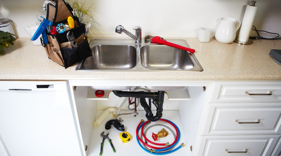 Kitchen sink with plumbing tools, including a toolbox, wrenches, and plumbing pipes, emphasizing smart maintenance for preventing holiday plumbing emergencies.